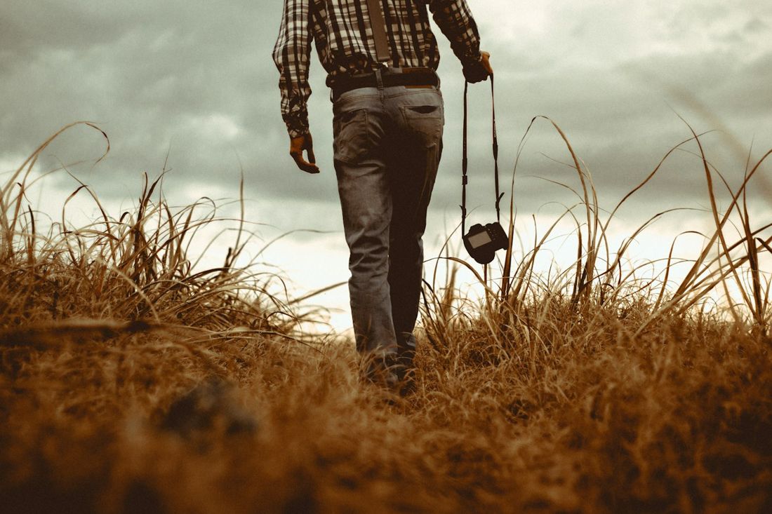 A photographer walking through tall dry grass with a camera