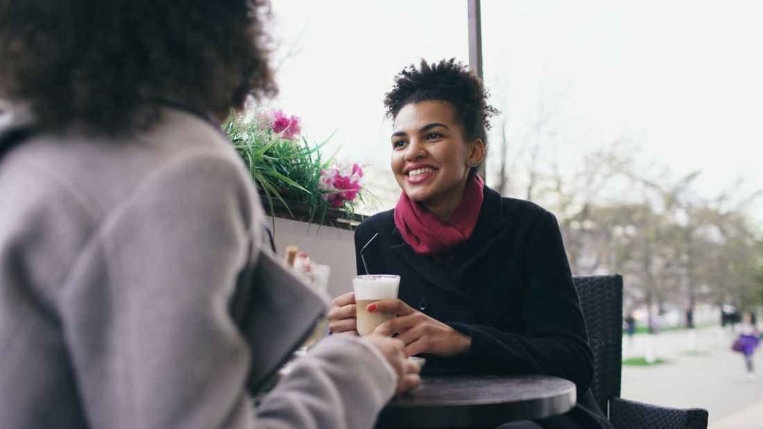 Two women talking and laughing over coffee at a café table