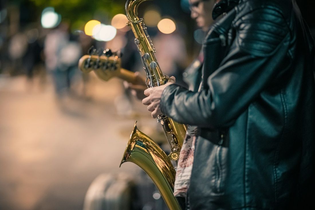 A saxophonist playing on a city street at dusk