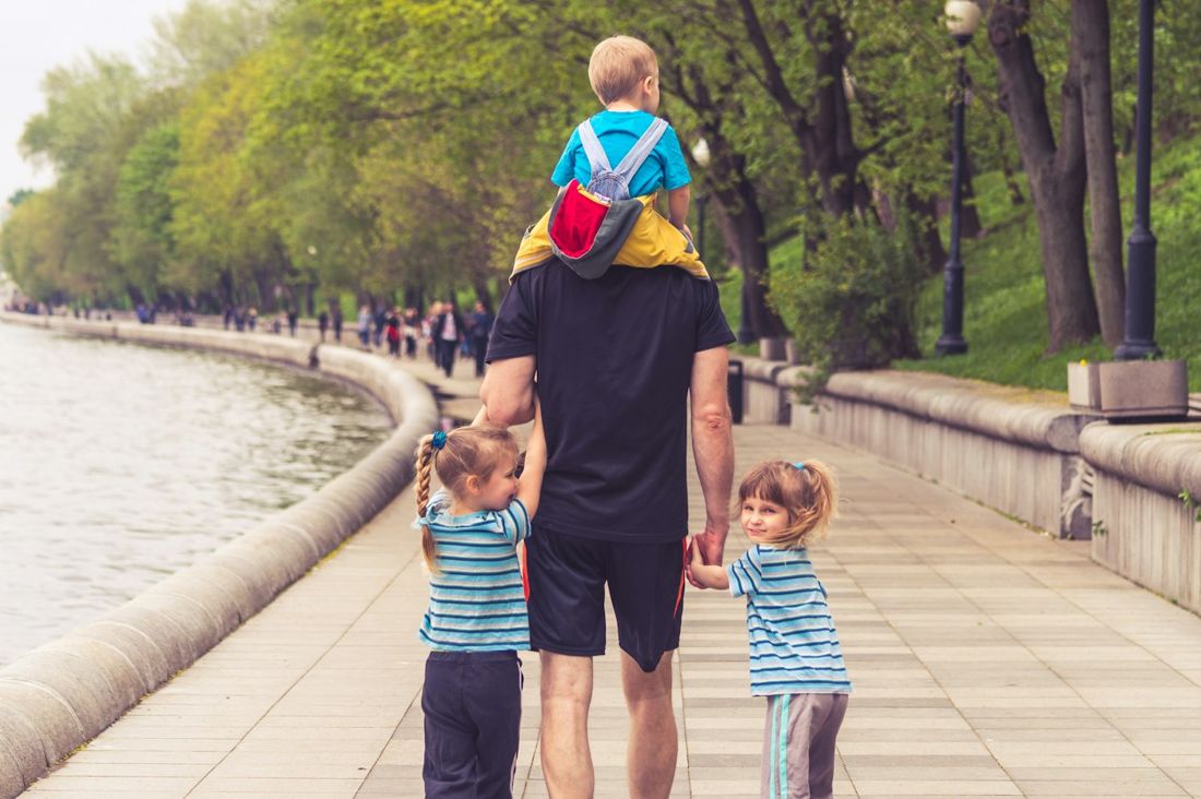A father walking with three children by a riverside path