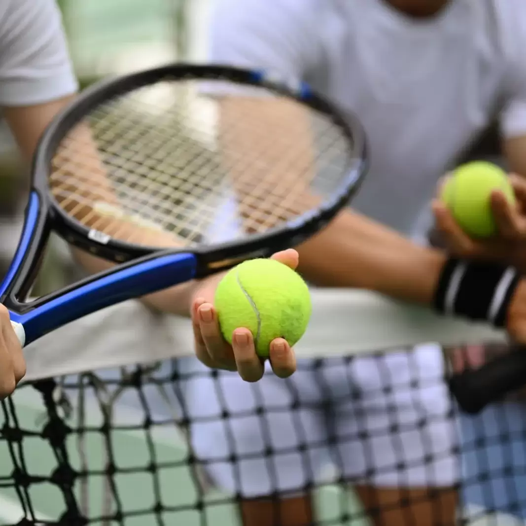 men-tennis-coach-giving-instructions-to-his-student-standing-by-net-at-the-outdoor-tennis-court
